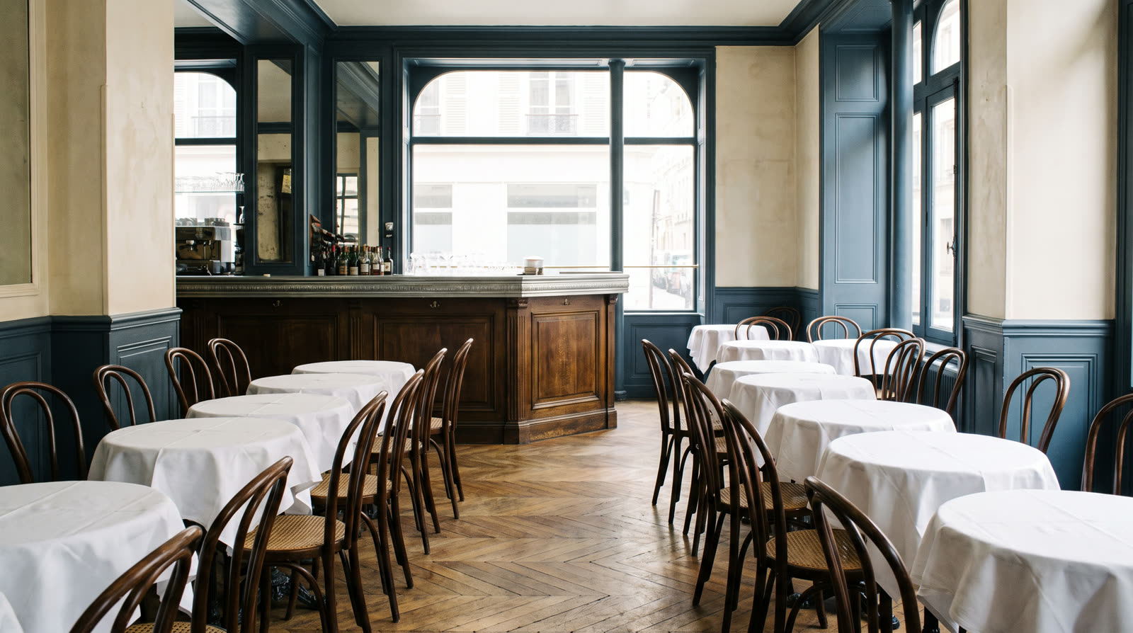 Salle de restaurant avant le service : tables dressées, comptoir en zinc et vitrine sur rue — salle, cuisine et réserve ne se pondèrent pas de la même façon.